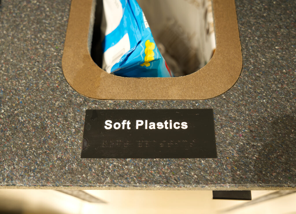 Soft plastics aperture with braille signage on the recycled material top
